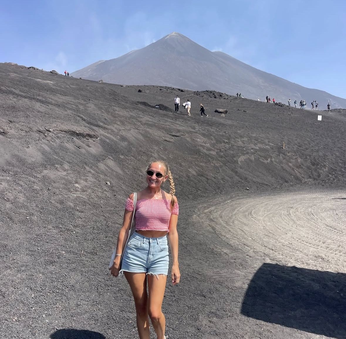Hiker in full volcanic gear with trekking poles crossing a black lava field near the summit craters