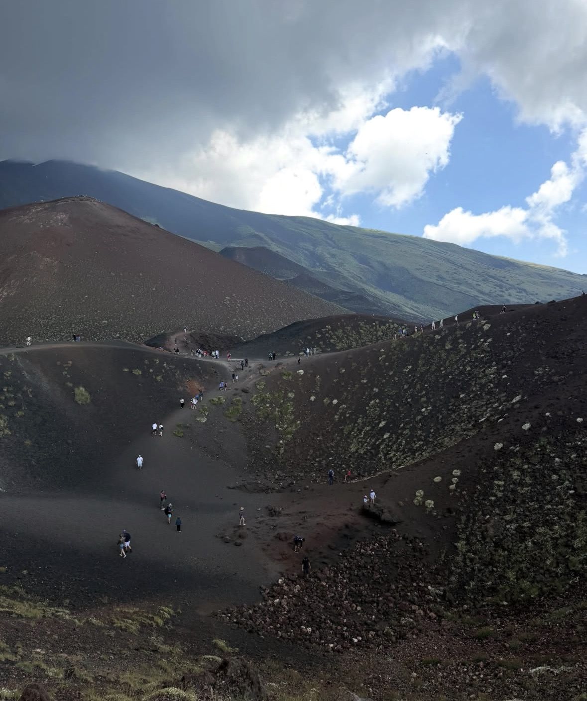Local Sicilian guide explaining volcanic geology to a small tour group on a lava flow with the crater in the background
